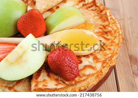 dessert : thin round pancake with honey strawberries and apple on wooden table