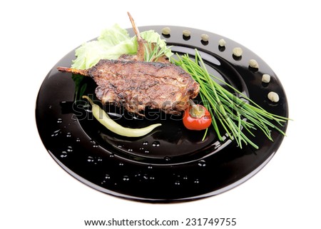 served main dish : lamb meat ribs on plate with hot peppers and capers on black plate isolated over white background