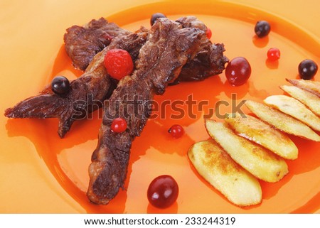 grilled beef meat with berries fried potatoes and cherry under sweet honey sauce on orange plate isolated over white background