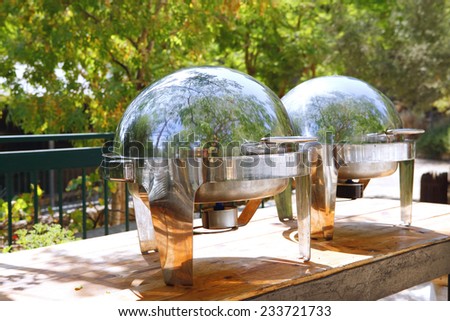 two closed stainless steel cloche on wooden table on restaurant outside party