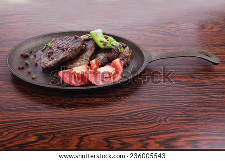 fresh roast beef fillet mignon on old retro style cast iron pan on retro wooden table as background with rosemary peppercorn and tomatoes