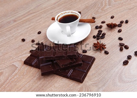 sweet hot drink : black Turkish coffee in small white mug with coffee beans spilled over a wooden table with stripes of dark chocolate and cinnamon stick