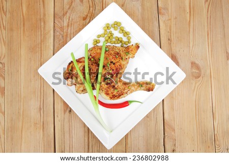 meat food : chicken legs garnished with green peas and hot chili peppers on white plates over wooden table
