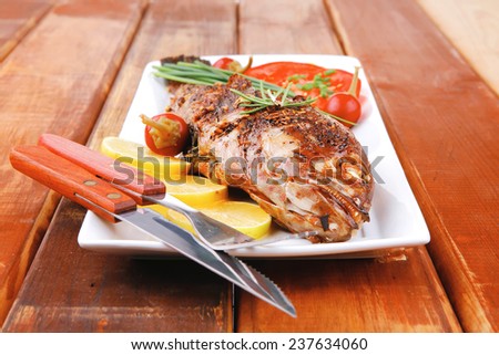 main course on wood: whole fried sunfish on plate with lemons and peppers