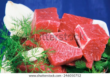 uncooked fresh beef meat chunks on white bowls with green hot peppers and vegetables serving over blue wooden table