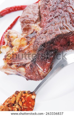 meat food : grilled beef steak served on white plate with red thin chili pepper and spices isolated over white background
