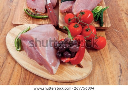fresh raw turkey meat steak fillet with vegetables kale tomatoes lettuce red hot chili pepper and dark olives on cutting board over wooden table