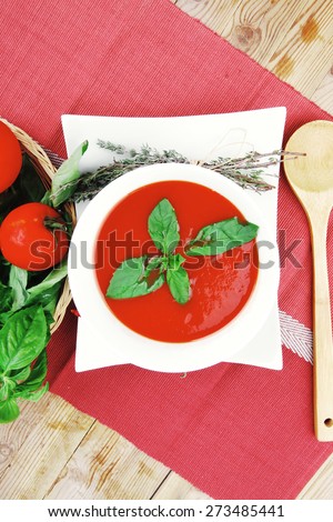 diet food : hot tomato soup with basil thyme and dry pepper in big bowl over red mat on wood table ready to eat