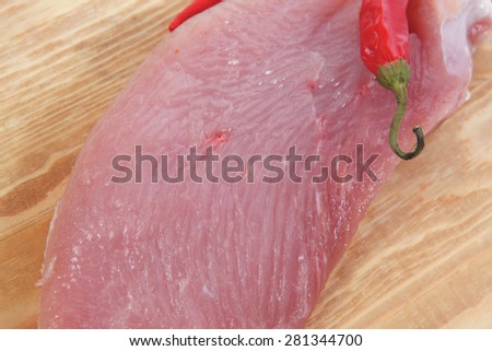 raw fresh turkey meat steak fillet cuts on wooden board with red hot chili pepper isolated over white background