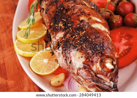 healthy lunch : whole fried sea sunfish on wooden table with lemons peppers and tomatoes and rosemary twig