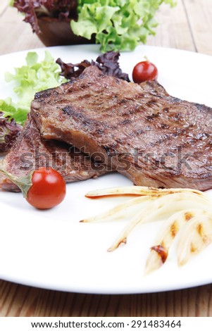 meat food : roast steak boneless with roast onion and red hot peppers, served on green lettuce salad on dish isolated over wooden table