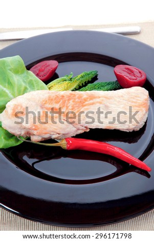 fresh roast turkey meat steak fillet with red hot pepper and green lettuce salad kale on black plate isolated over white background