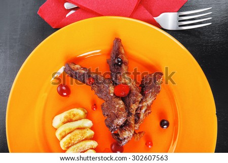 grilled beef meat with berries fried potatoes and cherry under sweet honey sauce on orange plate over black wooden table