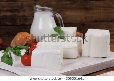 dairy food fresh white greek goat sheep feta cheese on plate with milk in pitcher cherry tomatoes french bun over dark wooden table