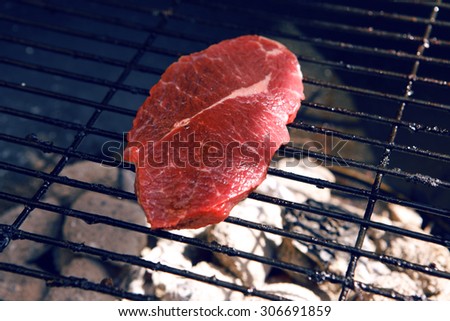 fresh raw beef fillet steak red meat on big round barbecue brazier black grid full burned charcoal