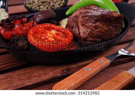 fresh roast bbq beef steak on black pan baked with mushroom potatoes tomatoes green hot chili pepper served with different peppercorn on dark wooden table