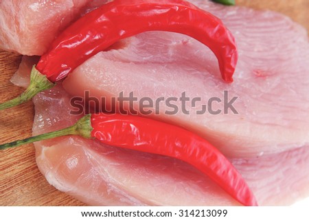 fresh raw turkey meat pieces on wooden cutting plate with red and green hot chili pepper isolated over white background