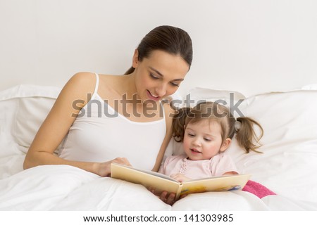 Happy mother and daughter reading a book together in bed