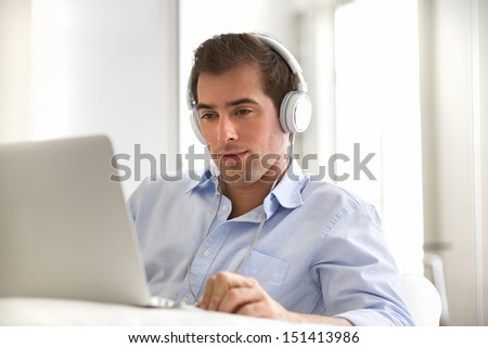 Man listening to music with Headphones on laptop computer, sitting on couch