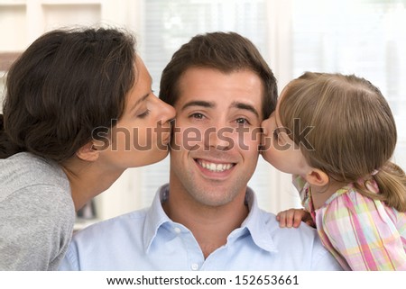Happy family, mother and daughter kissing father at home