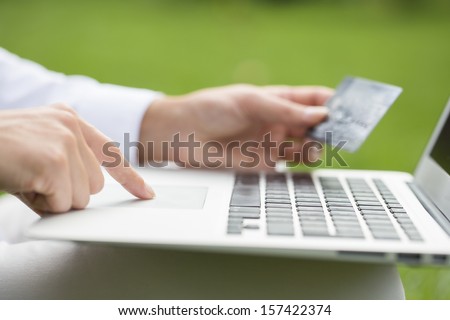 Close-up woman\'s hands holding a credit card and using computer keyboard for online shopping, outdoor