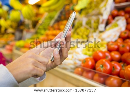 Woman using cell phone while shopping in supermarket, vegetable department store
