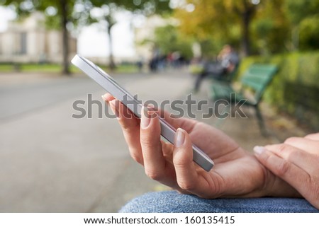 Woman with a cell phone, sitting in a park on a bench, reading a message, sms e-mail
