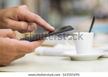 Man using a cell phone on cafe terrace, news paper and coffee
