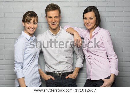 Portrait of 3 smiling students, isolated over a gray brick wall