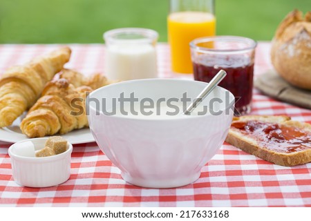Breakfast in garden with hot milk, orange juice, croissant, marmalade and bread.