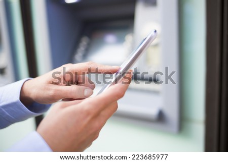 Woman using her mobile phone in front of a cash machine