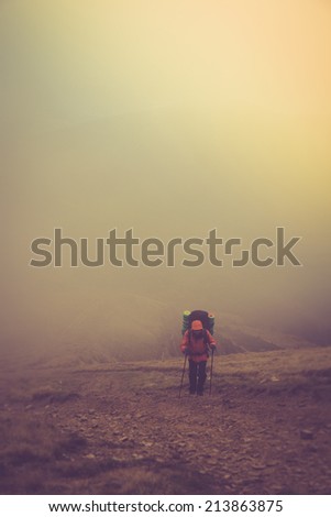 Tourists with backpacks climb to the top of the mountain in fog. Filtered image:cross processed vintage effect.