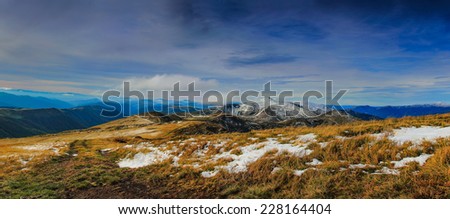Panoramic view mountain peaks and meadow with first autumn snow.