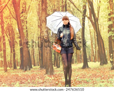 Beautiful girl with an umbrella walks in the park in the rain