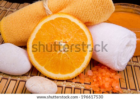 beautiful spa composition in orange colors of body scrub, bath towels and orange background on bamboo napkin