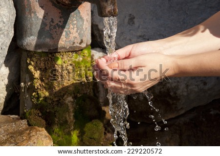 female hands under the column with a jet of cold water from the source