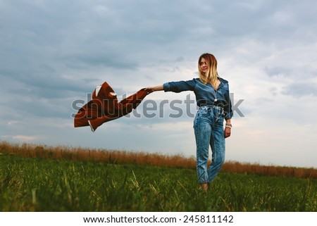 Beautiful fashionable girl in a field with a jacket in his hand