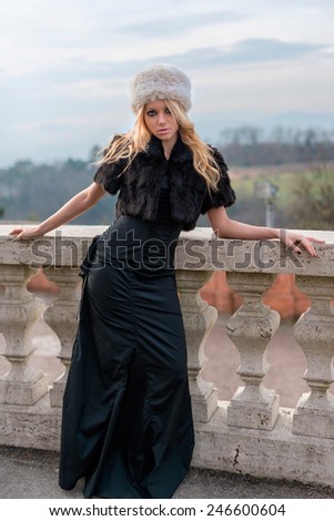 beautiful girl with blond hair and fur hat and a long black dress. Blond girl posing with hat and long dress
