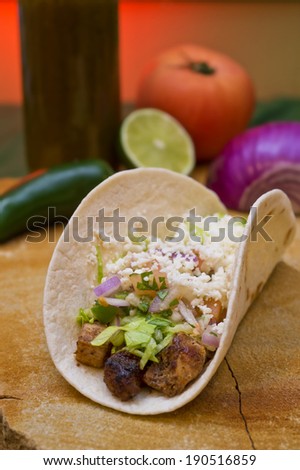 A soft taco with chicken, lettuce, tomato, onion, jalapeno hot peppers and hot sauce sits on a slab of red sandstone