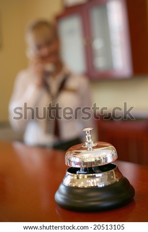 Metal and silver hotel bell, focus on the bell.Female receptionist in the background using a phone