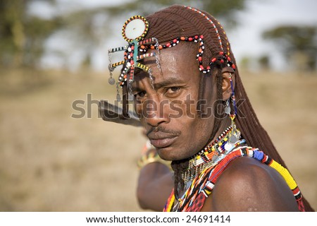 African Masai Warrior dressed in his traditional clothing. He is in the Masai Mara National Park wearing home-made Masai jewelry and his earlobes are stretched as is tradition with the Masai.