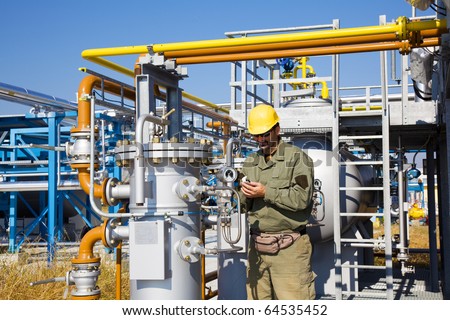 Engineer, oil-workers with large pipeline pump. refinery and pipelines in background. The best focus is on the device to the right side of workers.