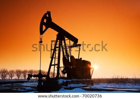 Oil field pumpjack silhouette with setting sun. Lens Flare.