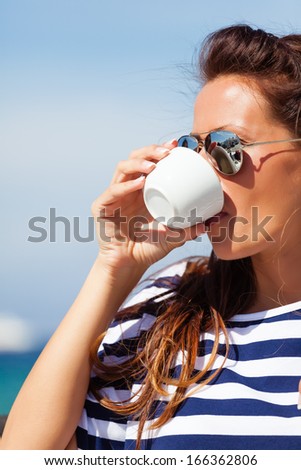 Beautiful woman sitting at a seaside cafe and drinks a coffee