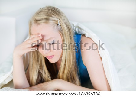 Young Woman holding her head in pain or sadness, lying in bed