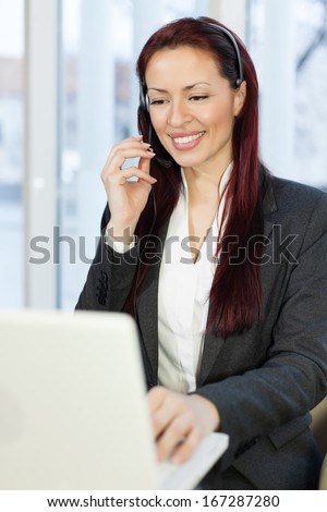 Woman with headphone talking and using a laptop computer