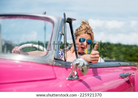 Happy woman in a pink convertible car, cabriolet, looking at camera, thumb up