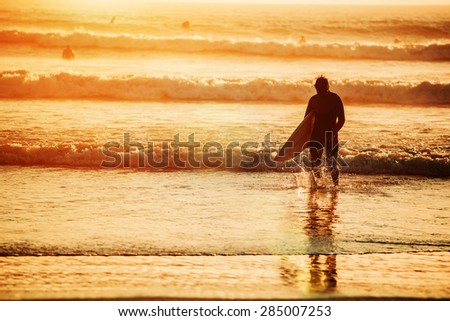 Silhouette of male surfer coming from a ocean waves,Sunset light, unrecognizable person, lens flare, copy space