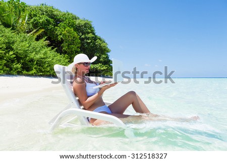 Woman resting on deck chair in turquoise water of white sand beach and using laptop.Copy space