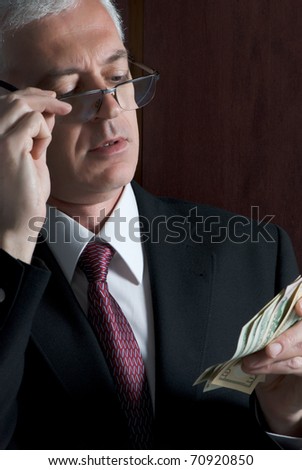 A crooked looking man counting a handful of dollar bills
